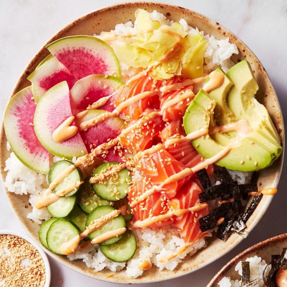 sushi rice in a bowl topped with salmon, cucumber, watermelon radish, sliced avocado, and spicy mayo