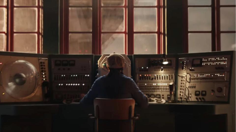 a person sits at a control panel surrounded by knobs and buttons