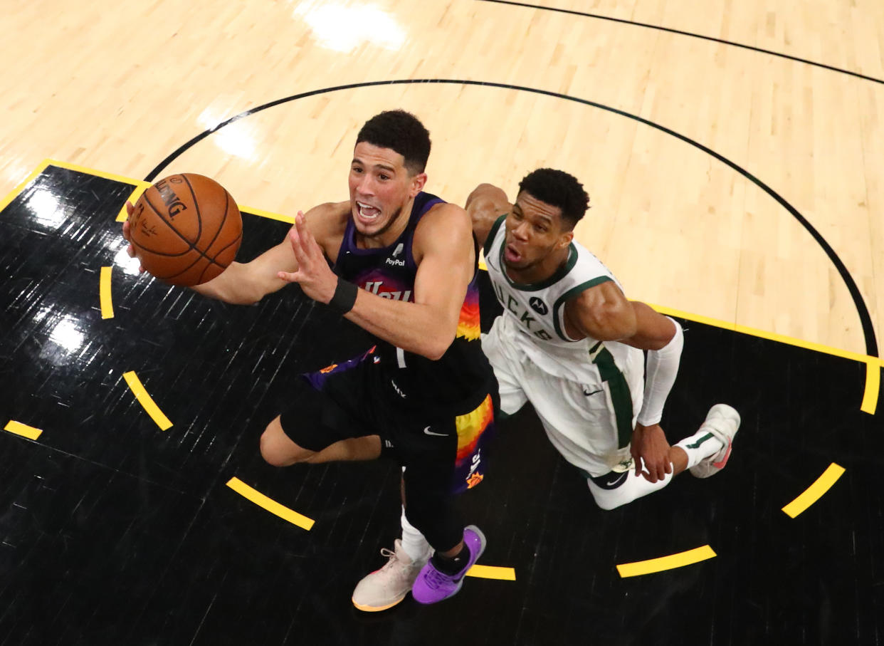 An overhead view of Devin Booker driving to the basket with Giannis Antetokounmpo trailing him.