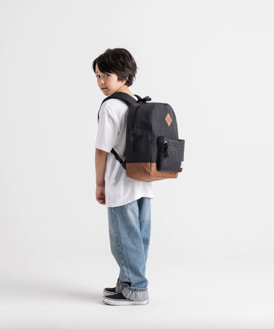 little boy wearing jeans, t-shirt, and black Herschel Heritage Backpack | Youth (photo via Herschel)