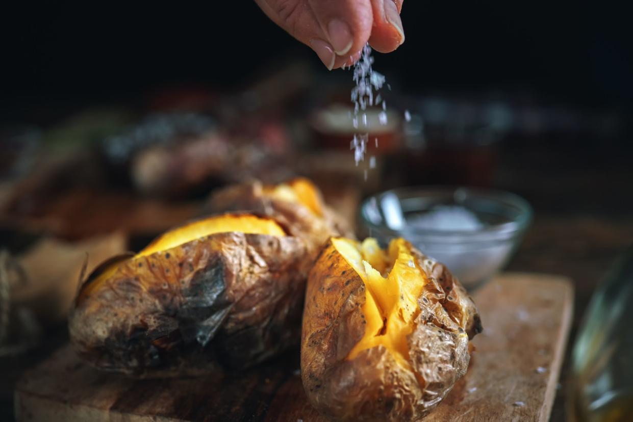 Closeup of hand seasoning two perfect baked potatoes with sea salt and olive oil with a blurred rustic background