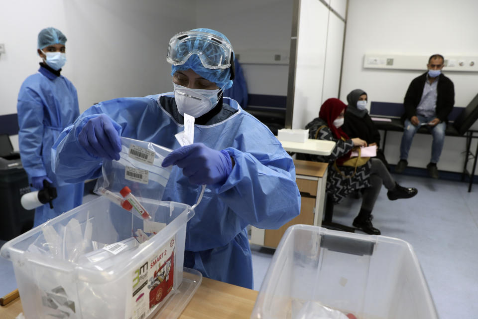 A nurse in protective clothing holds coronavirus testing material, at a center in the Rafik Hariri University Hospital in Beirut, Lebanon, Monday, Jan. 11, 2021. Lebanon's caretaker prime minister said Monday the country has entered a "very critical zone" in the battle against coronavirus as his government mulls tightening nationwide lockdown announced last week. (AP Photo/Bilal Hussein)