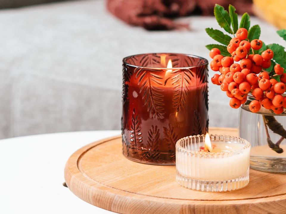 Two candles on a tray with faux berries and gray couch in background