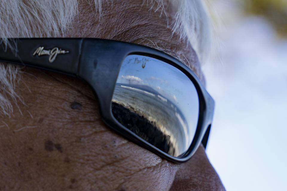 Lanai can be seen through the reflection of Abraham "Snake" Ah Hee's sunglasses at Launiupoko Beach Park on Friday, Feb. 23, 2024, in Lahaina, Hawaii. (AP Photo/Mengshin Lin)