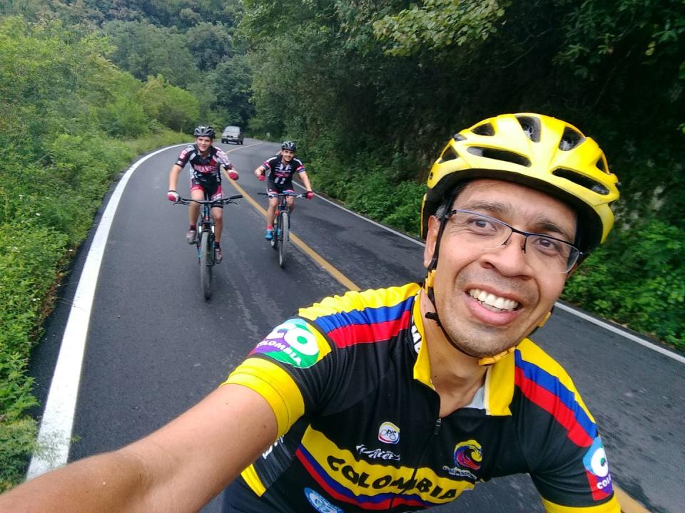 a cyclist takes a selfie on a mountain road with two other riders