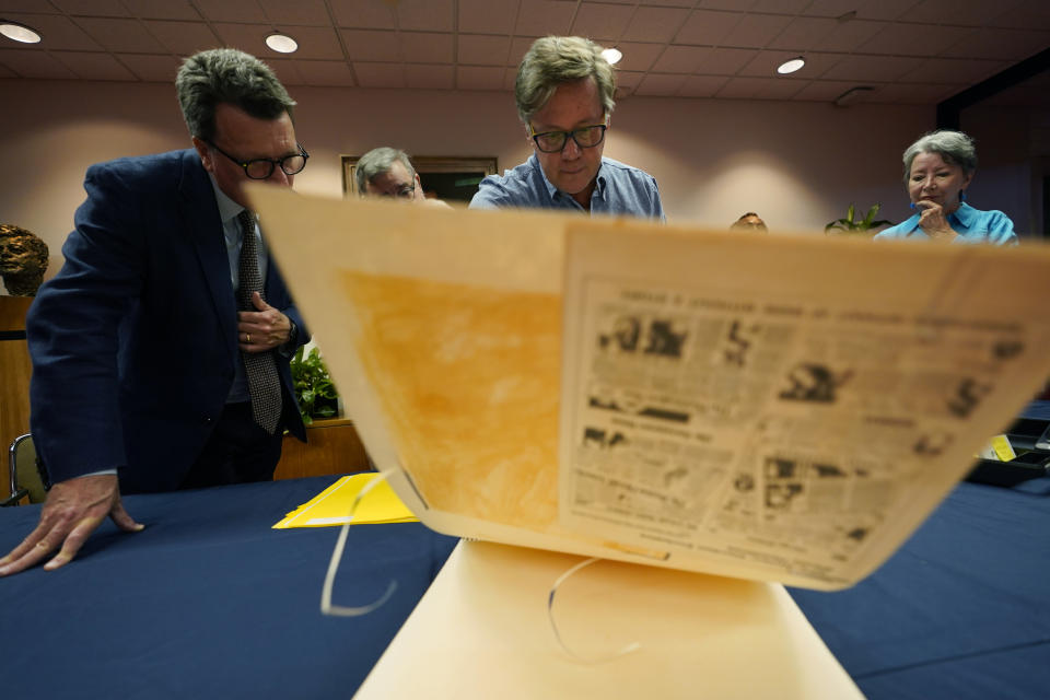 CORRECTS ID TO LIBRARY DIRECTOR MARK LAWRENCE INSTEAD OF LIBRARY STAFF ARCHIVIST BRIAN MCNERNEY - Peter Mangan, center, and his wife, Karen, right, look through a large folder of newspaper clippings at the Lyndon B. Johnson's presidential library with LBJ Library director Mark Lawrence, left, Wednesday, Aug. 31, 2022, in Austin, Texas. The family of late Associated Press reporter James W. Mangan has donated to the library cassette tapes containing interviews the reporter did that led to a 1977 story in which a Texas voting official detailed how three decades earlier, votes were falsified to give Johnson a slim victory in a U.S. Senate primary. (AP Photo/Eric Gay)