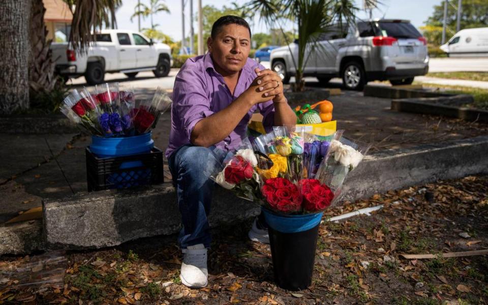 Street vendor Eddy Rivera poses with his wares in a shaded parking lot near the intersection where he works.