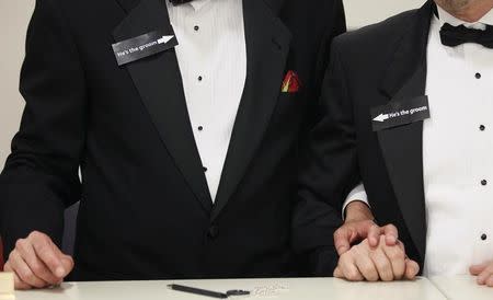 Two men, both wearing signs that read "he's the groom", hold hands shortly after midnight after getting a civil union when Colorado's civil union law went into effect in Denver May 1, 2013. REUTERS/Rick Wilking