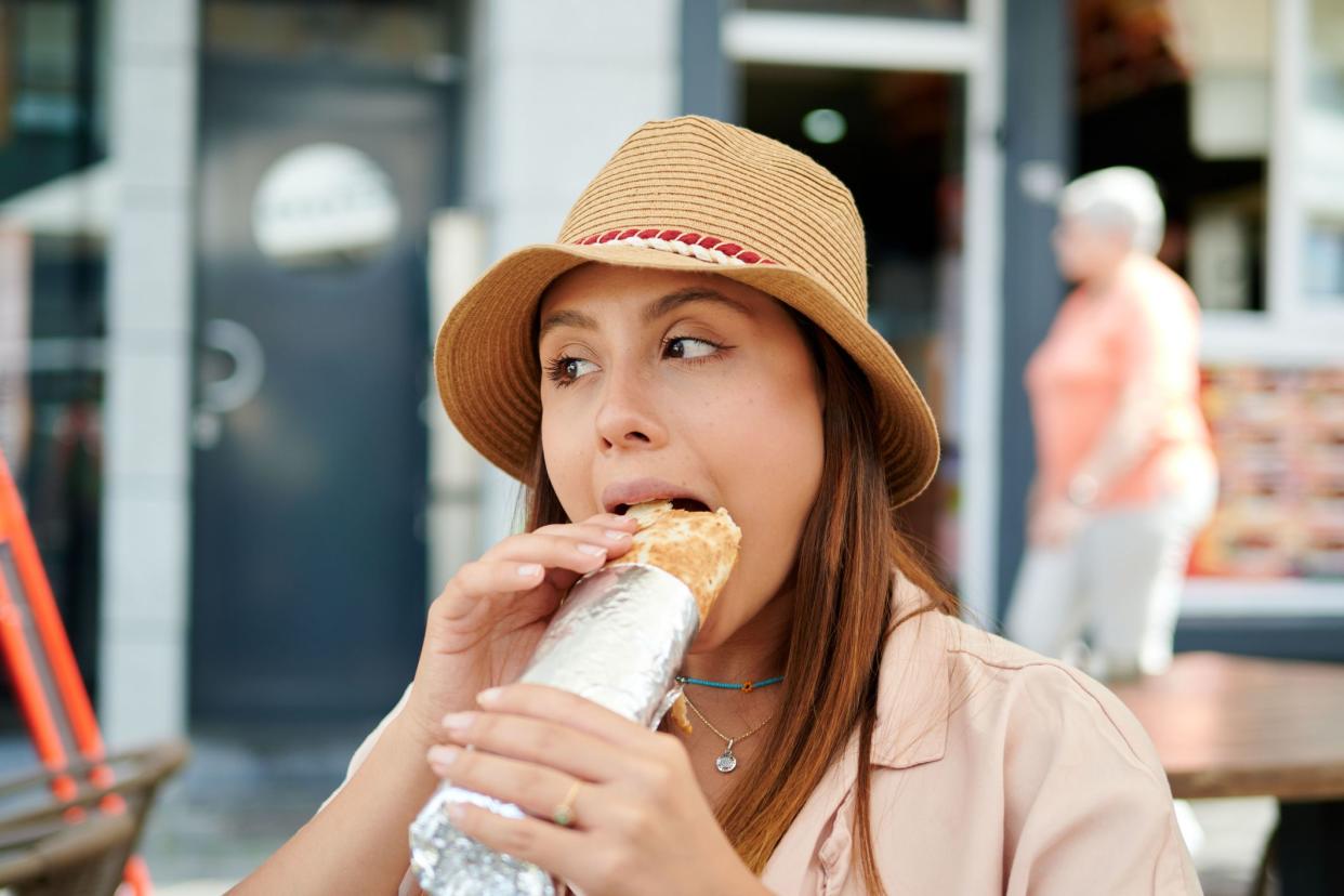 A female in a hat eating a burrito in a street cafe