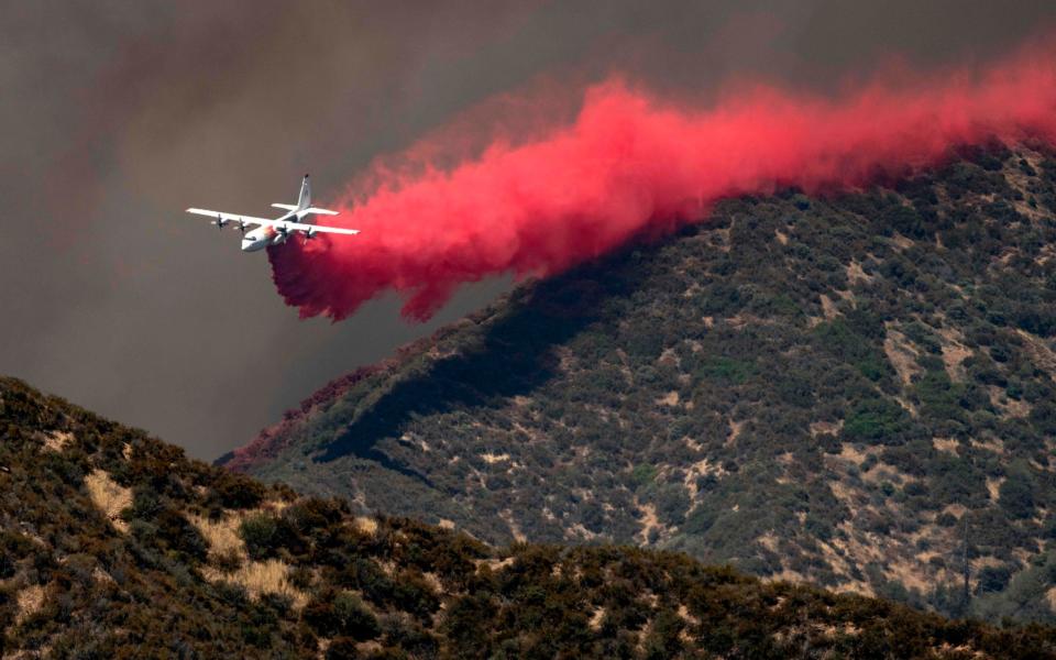 A firefighting plane makes a low-flying retardant drop on a ridge as firefighters continue to battle the Apple Fire - JOSH EDELSON/AFP