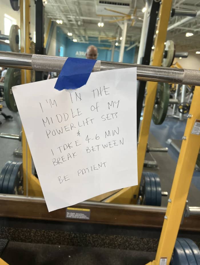 Handwritten note on gym equipment requesting patience for 4-6 minute breaks between powerlifting sets