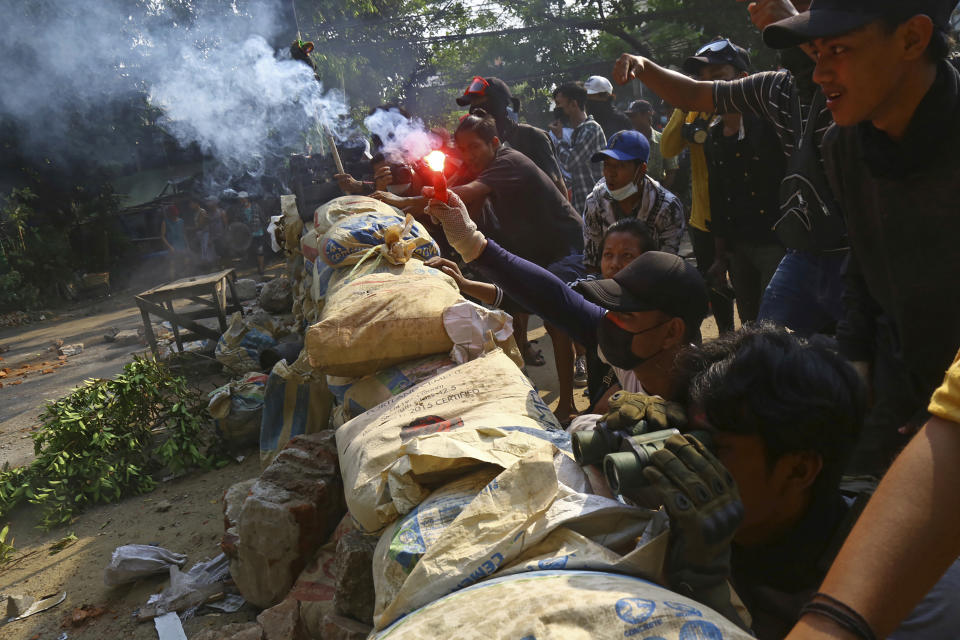 An anti-coup protester holds a smoke bomb behind makeshift barricade, as the protesters confront police in Yangon, Myanmar Sunday, March 28, 2021. Protesters in Myanmar returned to the streets Sunday to press their demands for a return to democracy, just a day after security forces killed more than 100 people in the bloodiest day since last month's military coup. (AP Photo)