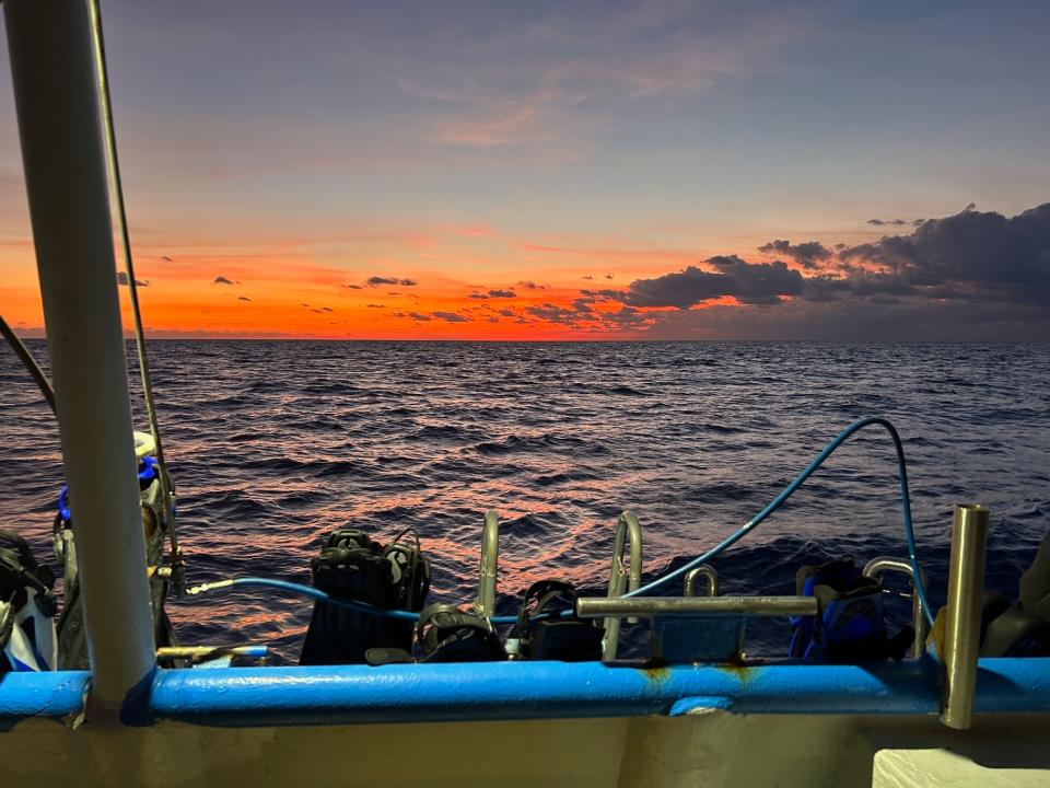 A view from a boat deck at sunset with scuba diving equipment in the foreground and the ocean extending to the horizon