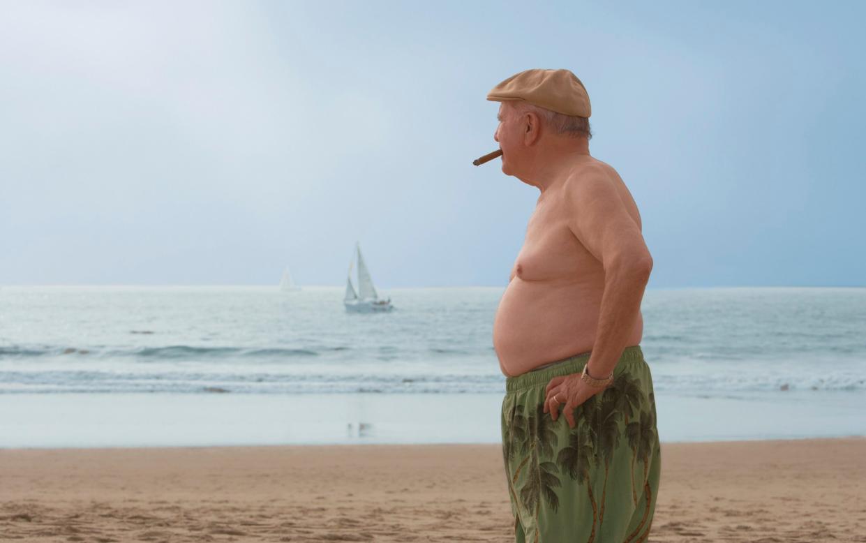 Man on beach smoking with fat belly