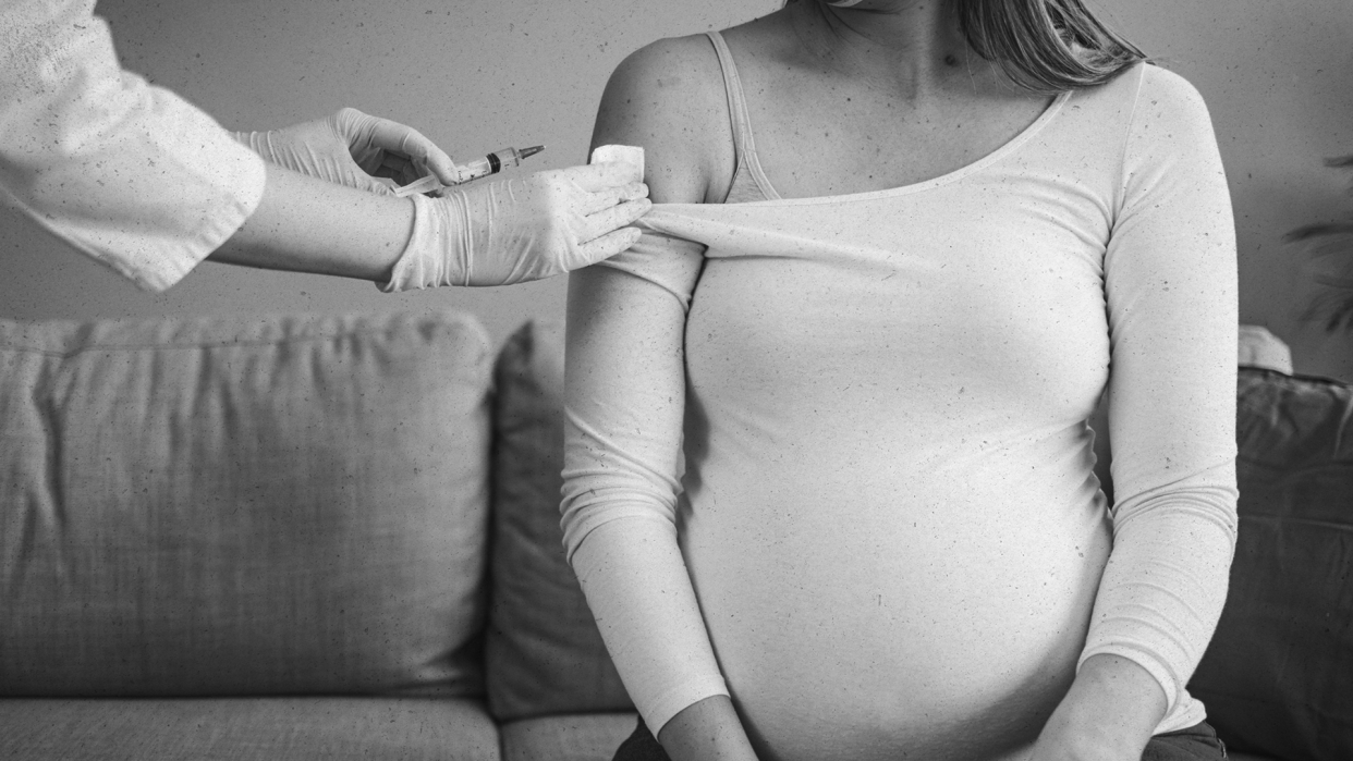 A pregnant woman about to receive a COVID vaccine in her arm.
