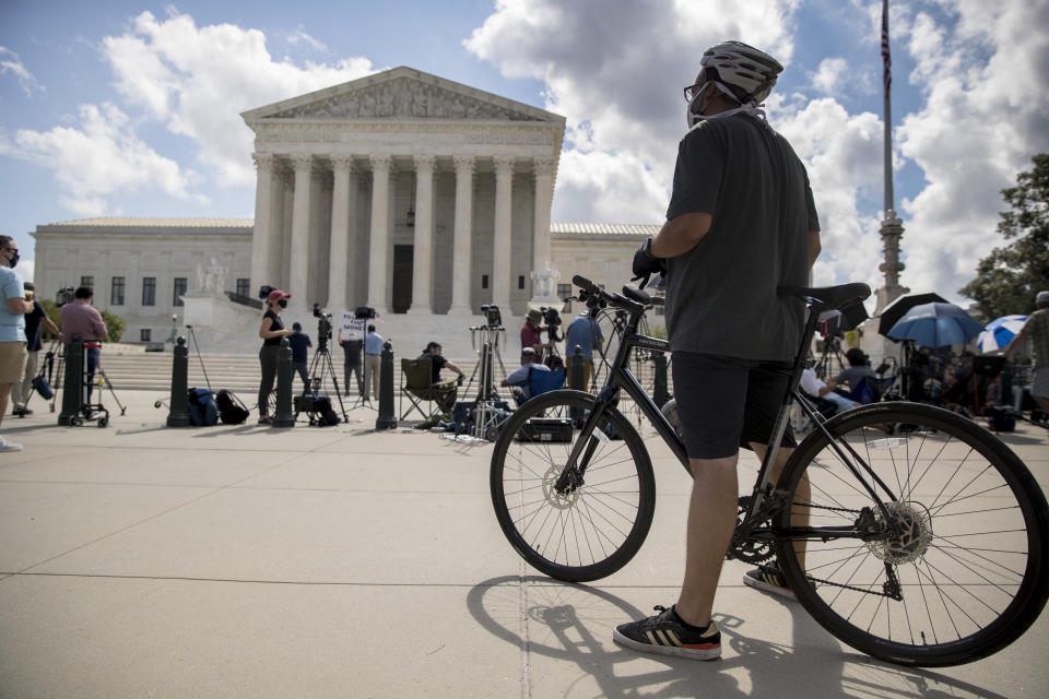 A man on a bicycle and members of the media stand outside the Supreme Court, Thursday, July 9, 2020, in Washington. The Supreme Court ruled Thursday that the Manhattan district attorney can obtain Trump tax returns while not allowing Congress to get Trump tax and financial records, for now, returning the case to lower courts. (AP Photo/Andrew Harnik)