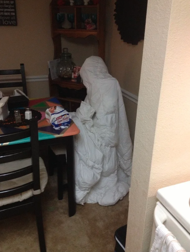 A down comforter tossed on top of a dining chair in the shape of a human