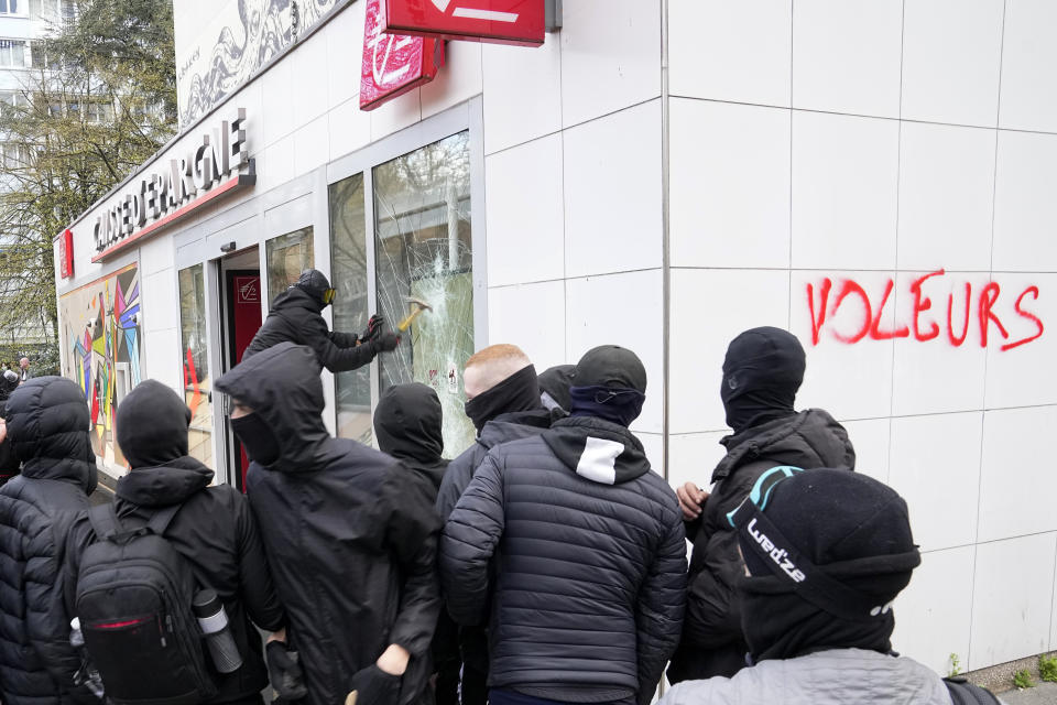 Un joven rompe la ventana de un banco durante una protesta el jueves 6 de abril de 2023, en París. (AP Foto/Michel Euler)