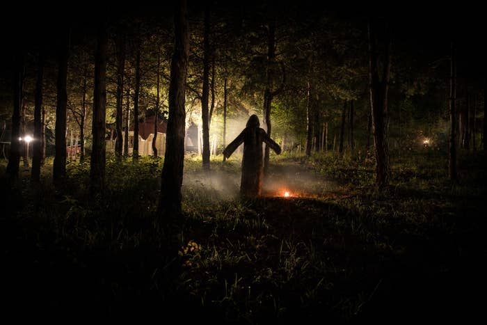 Silhouette of person standing in the dark forest with light