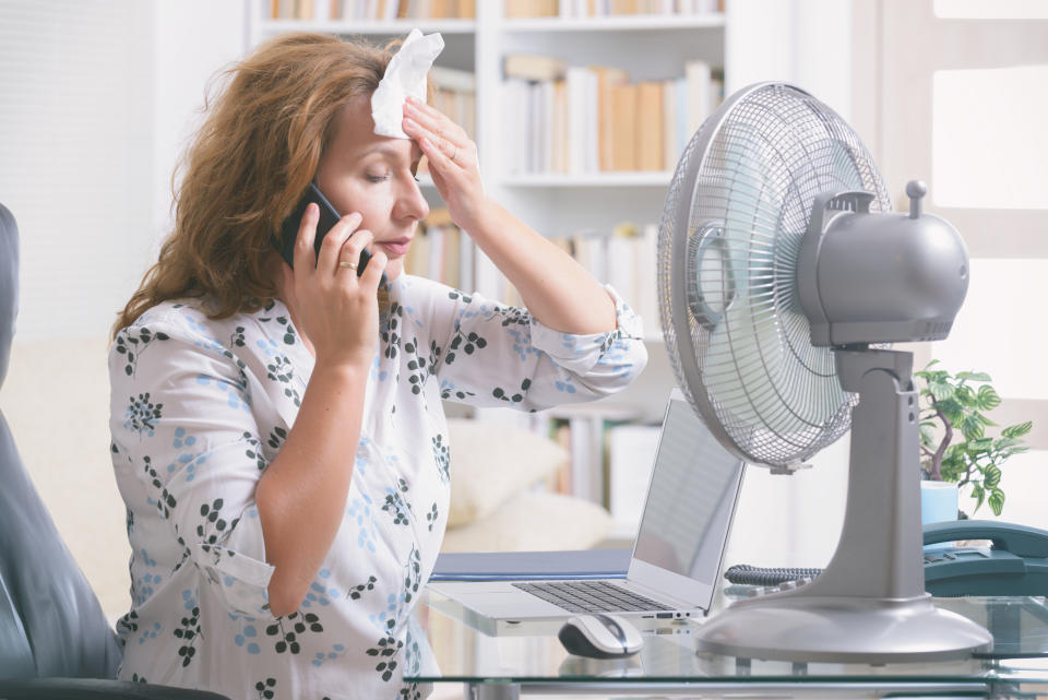 woman using a fan at her desk to cope with a hot flash