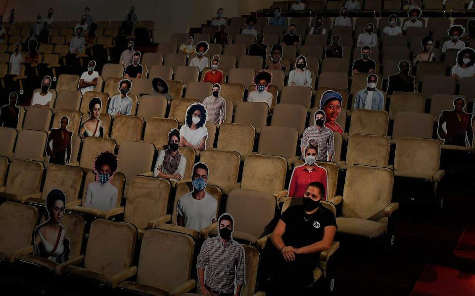 A woman sits near cardboard cutouts of people that will be used for social distancing in the theater, during a general rehearsal at the Teresa Carreno Theater in Caracas, Venezuela - Matias Delacroix/AP