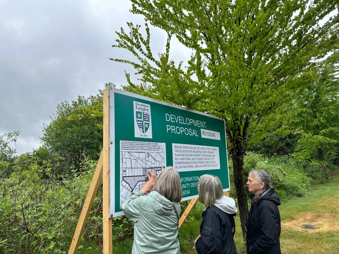 Residents examine a sign outlined the proposed re-zoning of 37.23 hectares (92 acres) of the West Creek watershed area to make way for 14.97 hectares (37 acres) of industrial development in Langley, B.C. on June 10, 2023. (Yasmin Gandham/CBC - image credit)