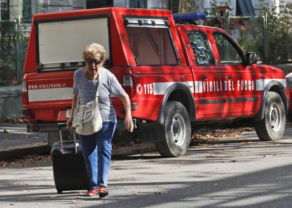 A woman pulls a suitcase after being accompanied by firefighters to get her belongings from her home, in Genoa, Italy, Thursday Aug. 16, 2018. Authorities worried about the stability of remaining large sections of a partially collapsed bridge evacuated about 630 people from nearby apartments, some practically in the shadow of the elevated highway. (AP Photo/Antonio Calanni)