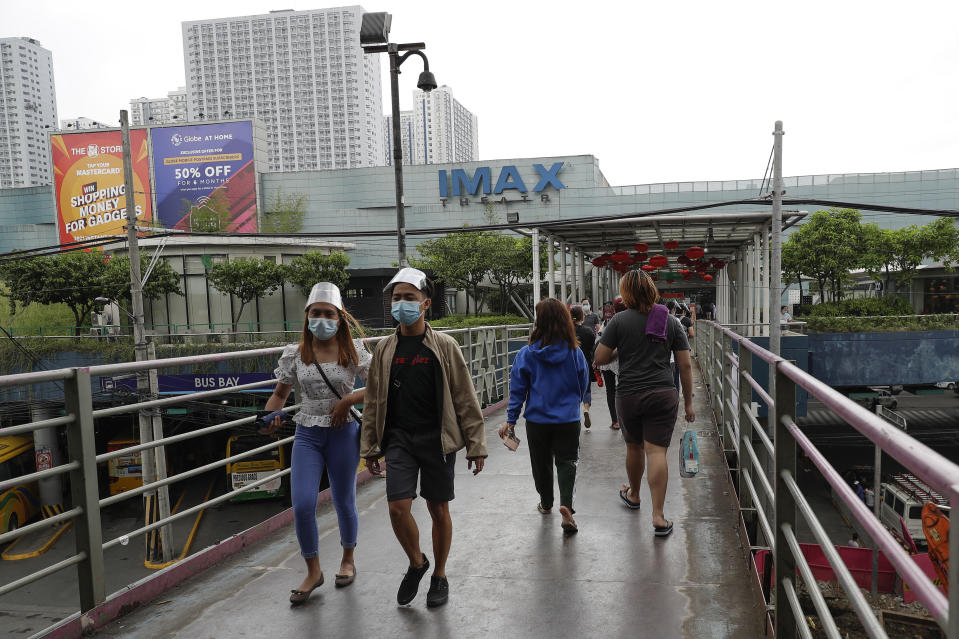 People wearing face mask and shield to prevent the spread of the coronavirus walk outside a mall that houses movie theaters in Quezon City, Philippines on Monday, Feb. 15, 2021. The Philippine government's approval for reopening many movie theaters, video game arcades and other leisure businesses closed since last year was postponed at least another two weeks after mayors feared it will bring new coronavirus infections. (AP Photo/Aaron Favila)