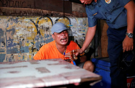 A police officer gives a glass of water to a man as he comforts him after his brother, who police say was killed in a spate of drug-related violence overnight, was shot in Manila, Philippines August 16, 2017. REUTERS/Dondi Tawatao