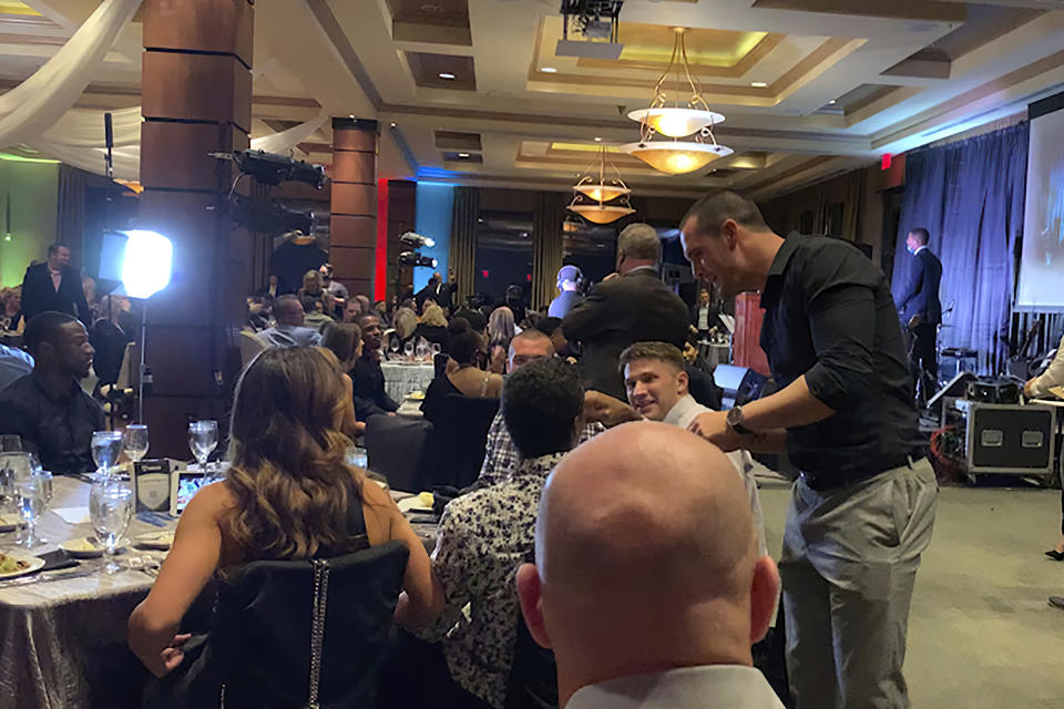 People sit at a table without masks. Derek Carr signs an autograph, also without a mask. 