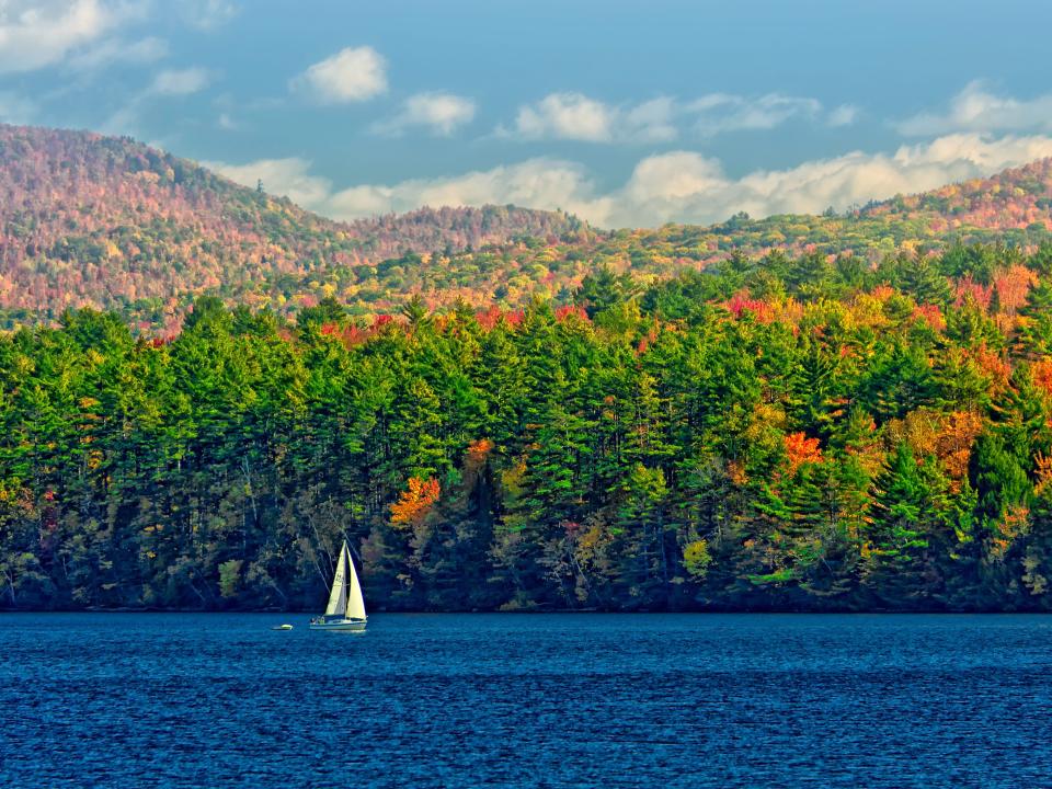 A sailboat on Vermont's Lake Champlain with fall foliage in the background.