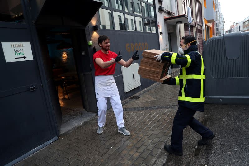 Pizza maker Russo hands Carrero Castano, a delivery man for the Spanish postal service “Correos”, some of the 40 pizzas that Grosso Napoletano restaurant donates daily to medical staff at hospitals as part of the Food4Heroes initiative