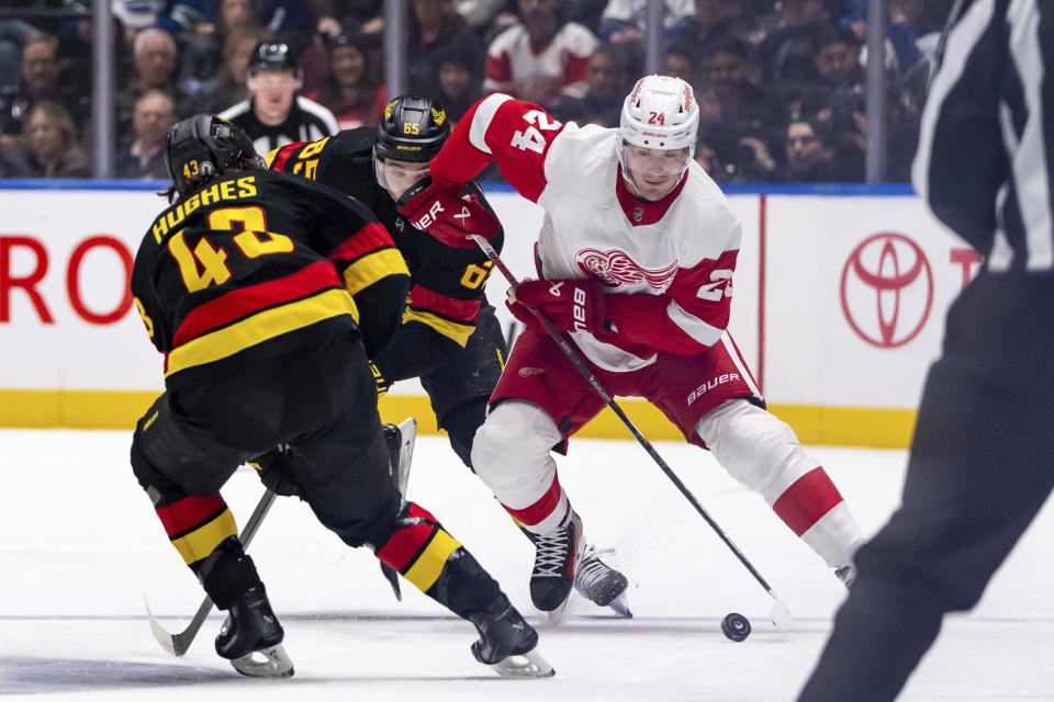 Vancouver Canucks' Ilya Mikheyev (65) and Detroit Red Wings' Klim Kostin (24) vie for the puck as Canucks' Quinn Hughes (43) defends during the second period of an NHL hockey game Thursday, Feb. 15, 2024, in Vancouver, British Columbia. (Ethan Cairns/The Canadian Press via AP)