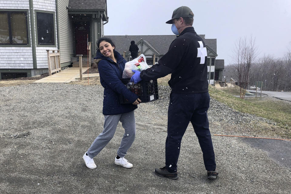 In this Monday, April 13, 2020 photo provided by Jay Peak Resort, Antonella Atto, left, from Peru, receives a week's supply of food from David Marchand, resort ski patrol director, in Jay, Vt. She is among hundreds of college students from South America working at U.S. ski resorts during what was their college summer break, who are unable to return home because of the COVID-19 coronavirus pandemic. (Melissa Sheffer/Jay Peak Resort via AP)