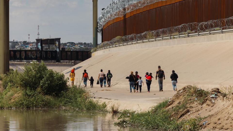 A group of migrants from Venezuela walk between the southern border wall and the Rio Grande river towards a temporary border patrol processing facility on Oct. 6, 2022 in El Paso, TX. (Jordan Vonderhaar for The Texas Tribune)