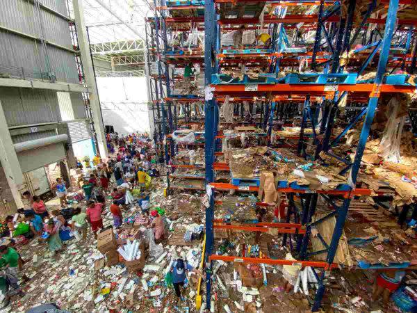 Ante la desesperación por no tener alimento y ni agua, personas buscan qué comer y qué artículos llevar en lo que queda de una tienda. 