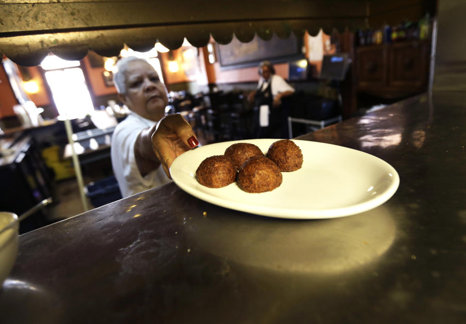 In this Monday, Jan. 28, 2013 photo, waitress Gaynell James serves up calas cake from the kitchen at The Old Coffeepot Restaurant in the French Quarter of New Orleans. Tired of celebrating Mardi Gras with the same old beignets? Make the switch to calas, tangy rice fritters born to go with cafe au lait. Calas (KAH-luhs) can be tough to find these days, but they have a rich history that spans the great cuisines of New Orleans. (AP Photo/Gerald Herbert)