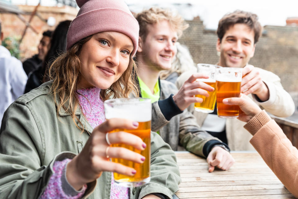 Friends drinking and toasting with beer at pub brewery - Beautiful young woman looking at camera and raising her pint glass - Lifestyle and drink concepts in London