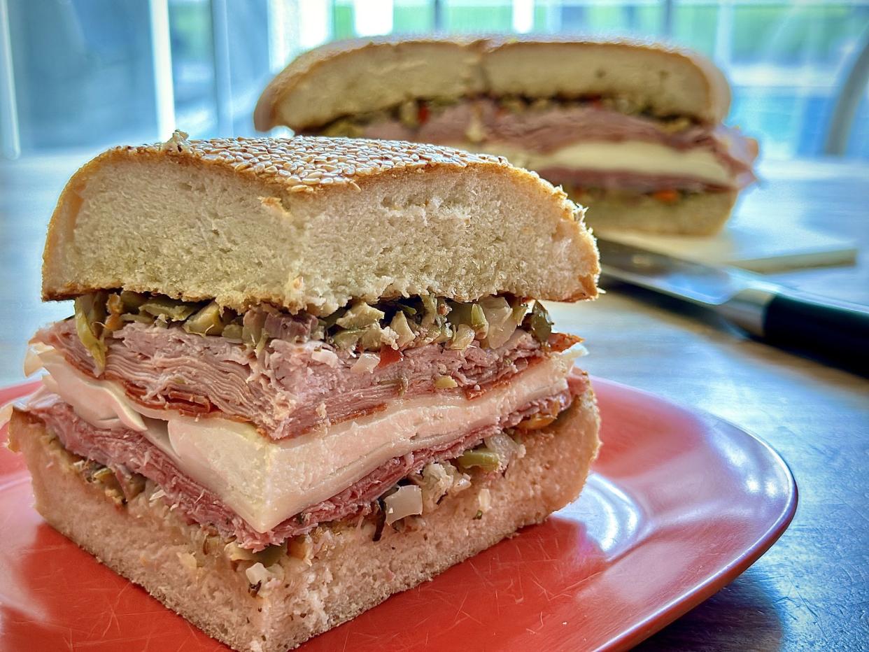 A giant muffuletta sandwich ready to be cut with a cleaver.