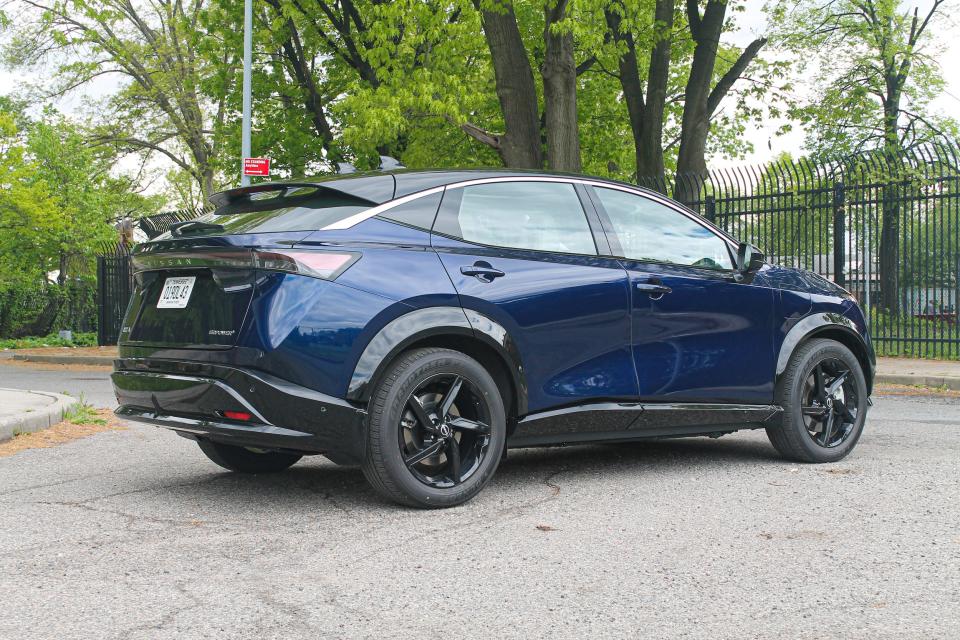 The blue 2023 Nissan Ariya Empower+ SUV is seen from the rear, with trees in the background.