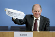 German Finance Minister Olaf Scholz holds a stack of files representing new laws in Berlin, Germany, Monday, March 23, 2020 during a joint press conference with German Economy Minister Peter Altmaier on the supplemental budget 2020 and how the ministries will react against the new coronavirus. For most people, the new coronavirus causes only mild or moderate symptoms. For some it can cause more severe illness (AP Photo/Michael Sohn, pool)