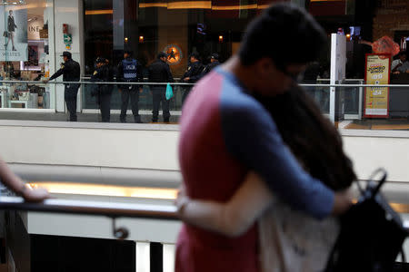 People watch police standing outside a footwear shop after a man shot a woman in the abdomen there before shooting himself in the head according to the police statement in Mexico City, Mexico March 19, 2018. REUTERS/Carlos Jasso