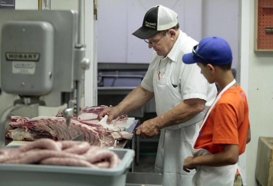 From left, Cliff’s Meat Market owner/operator Cliff Collins, 68, shows his grandson Ethan Truesdale how he slices fat off of slab of pork ribs and sidemeat while making fresh cuts of meat in his downtown Carrboro, NC butcher shop Wednesday, July 27, 2016.