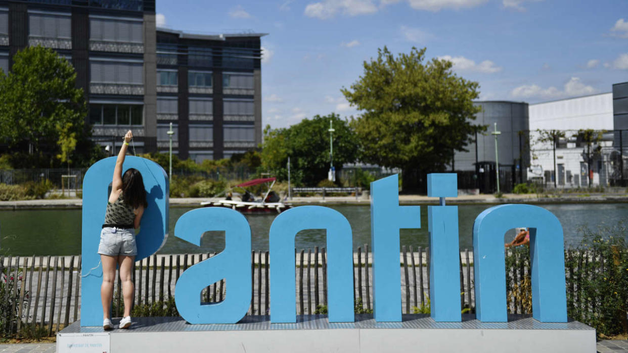 A young woman reaches above a sign of the city of 'Pantin' on the banks of the Canal de l'Ourcq at the Magasins Generaux place in Pantin, on July 30, 2022. - The canal de l'Ourcq celebrates this year the 200th anniversary of its inauguration. (Photo by JULIEN DE ROSA / AFP)