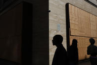 Pedestrians are silhouetted as they walk past a shop boarded up with plywood panels to protect the building against potential vandalism and looting Wednesday, June 3, 2020, in downtown Los Angeles, as protests continue over the death of George Floyd on May 25 in Minneapolis. Los Angeles County pushed back the start of its curfew from 6 p.m. to 9 p.m., a help to newly reopened restaurants and retail stores that were shut down for weeks by anti-coronavirus orders. (AP Photo/Jae C. Hong)