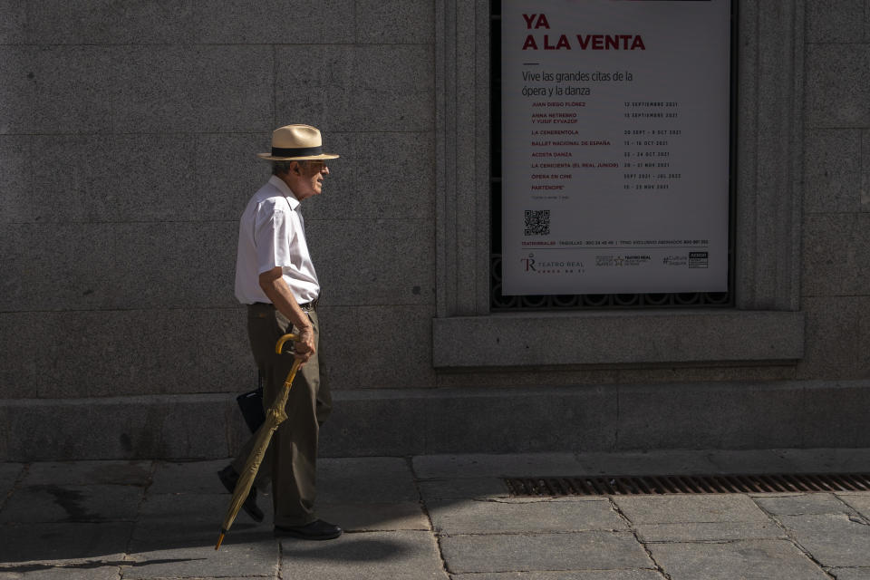 A man with a hat and an umbrella walks outside the Royal Theatre during a heatwave in Madrid, Spain, Friday, Aug. 13, 2021. Stifling heat is gripping much of Spain and Southern Europe, and forecasters say worse is expected to come. (AP Photo/Andrea Comas)