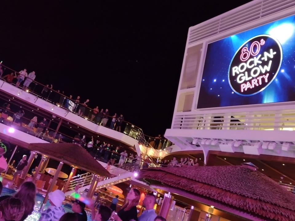 A crowded cruise ship top deck party with an '80s glow in the dark theme.