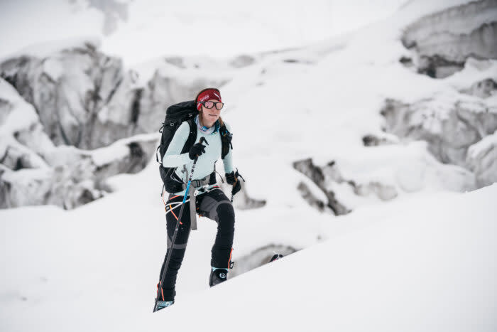 Tybor with skis and skins on, going up a snow ramp with seracs in background, on a cloudy day. 