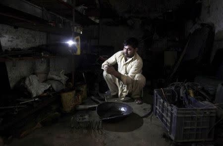 A mechanic cleans parts using light from a torch during a power outage in Lahore, Pakistan, November 6, 2015. REUTERS/Mohsin Raza