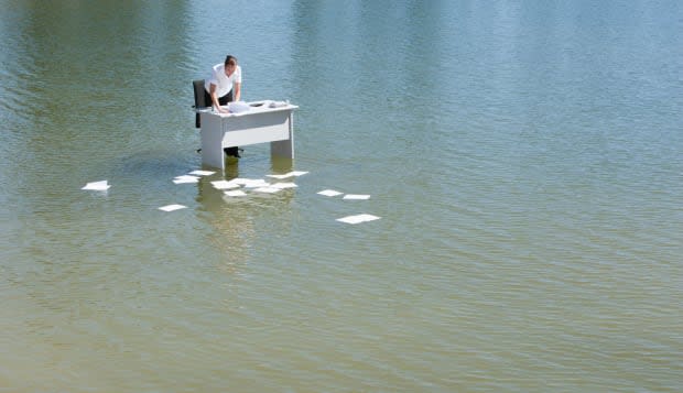 Businesswoman at desk in water with paperwork floating away